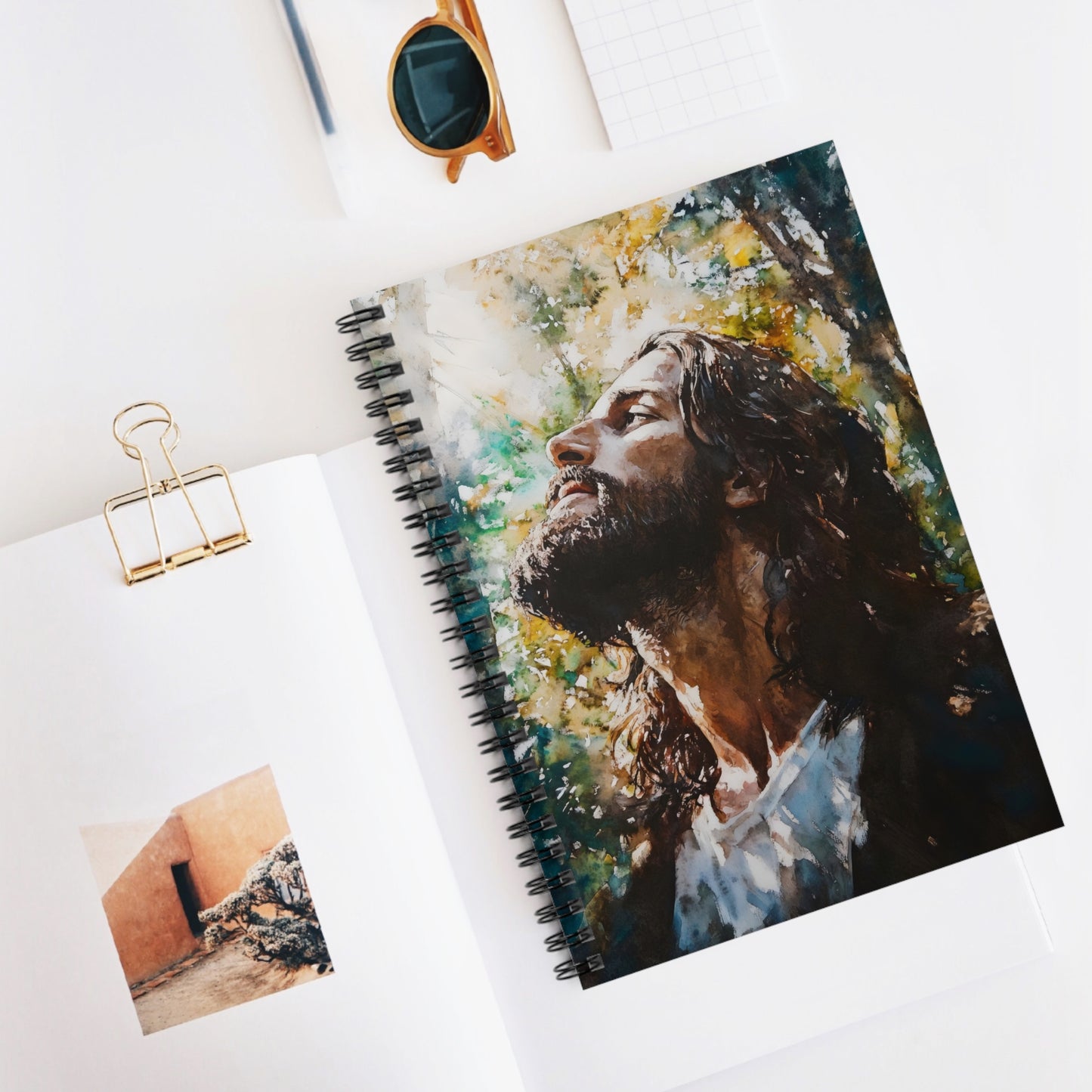 Christian spiral notebook with a watercolor painting of Jesus outdoors, on white desk