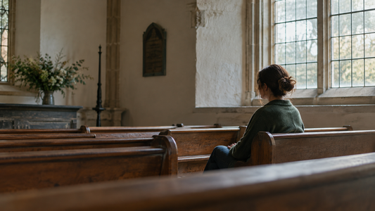 A woman sits alone in a simple church pew in soft daylight.