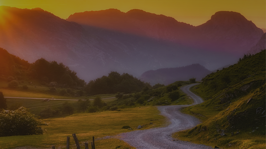 Peaceful winding path through green hills at sunrise, misty mountains in the distance