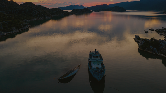 Serene lake at sunset with a boat and canoe, surrounded by mountains and rocky shoreline.