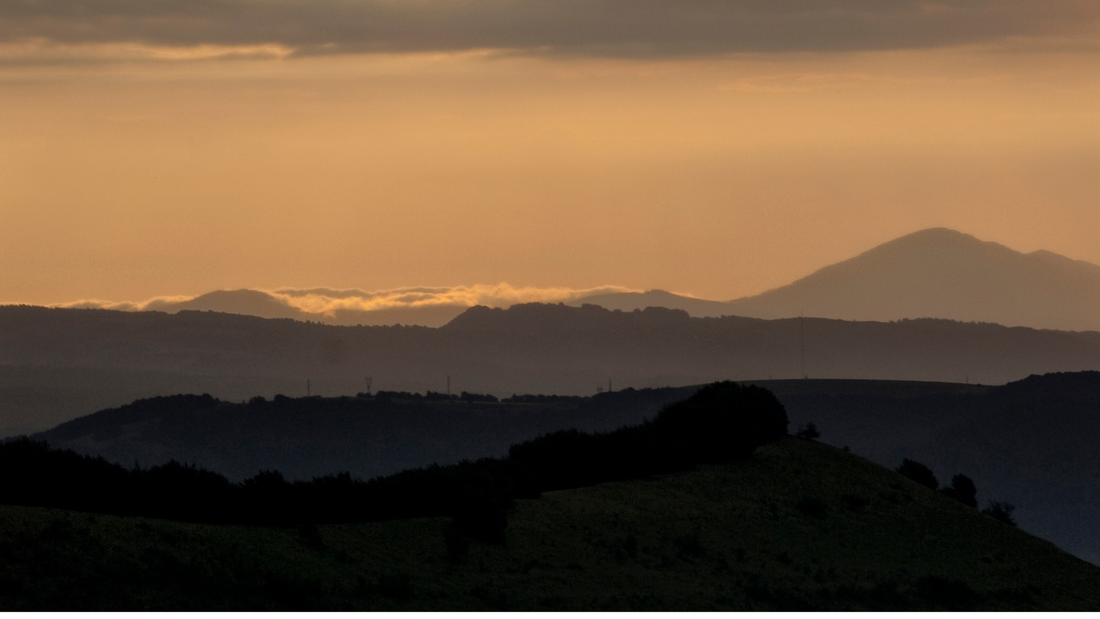 Serene mountain silhouette at sunrise with soft golden sky and layered hills
