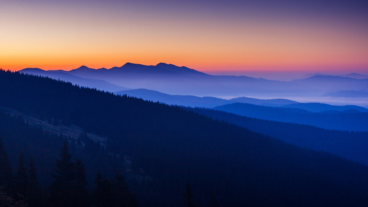Serene mountain landscape at sunrise with layered blue hills and orange twilight sky
