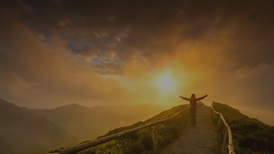 Silhouette of a person with arms outstretched on a mountain path at sunrise, serene landscape