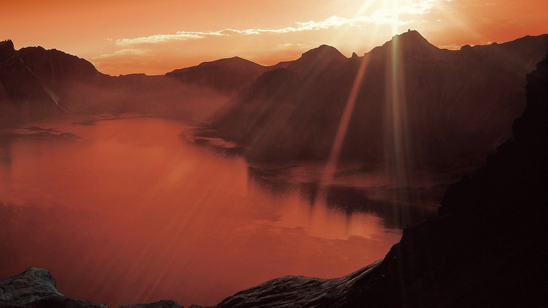 Sunrise over tranquil mountain lake with sun rays, peaceful nature landscape