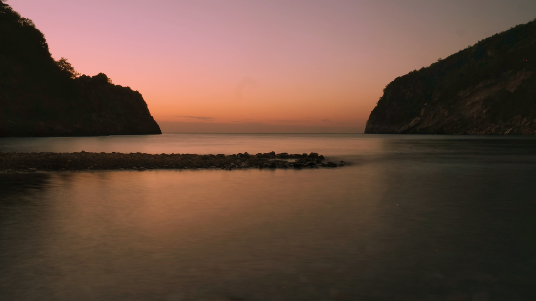 Peaceful sunset over calm sea with rocky shore and silhouettes of cliffs, tranquil landscape