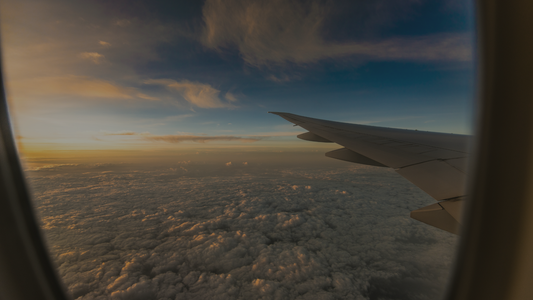 Airplane wing view above clouds at sunset through window, peaceful sky travel scene