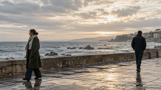 Two adults walk apart along a quiet coastal promenade.