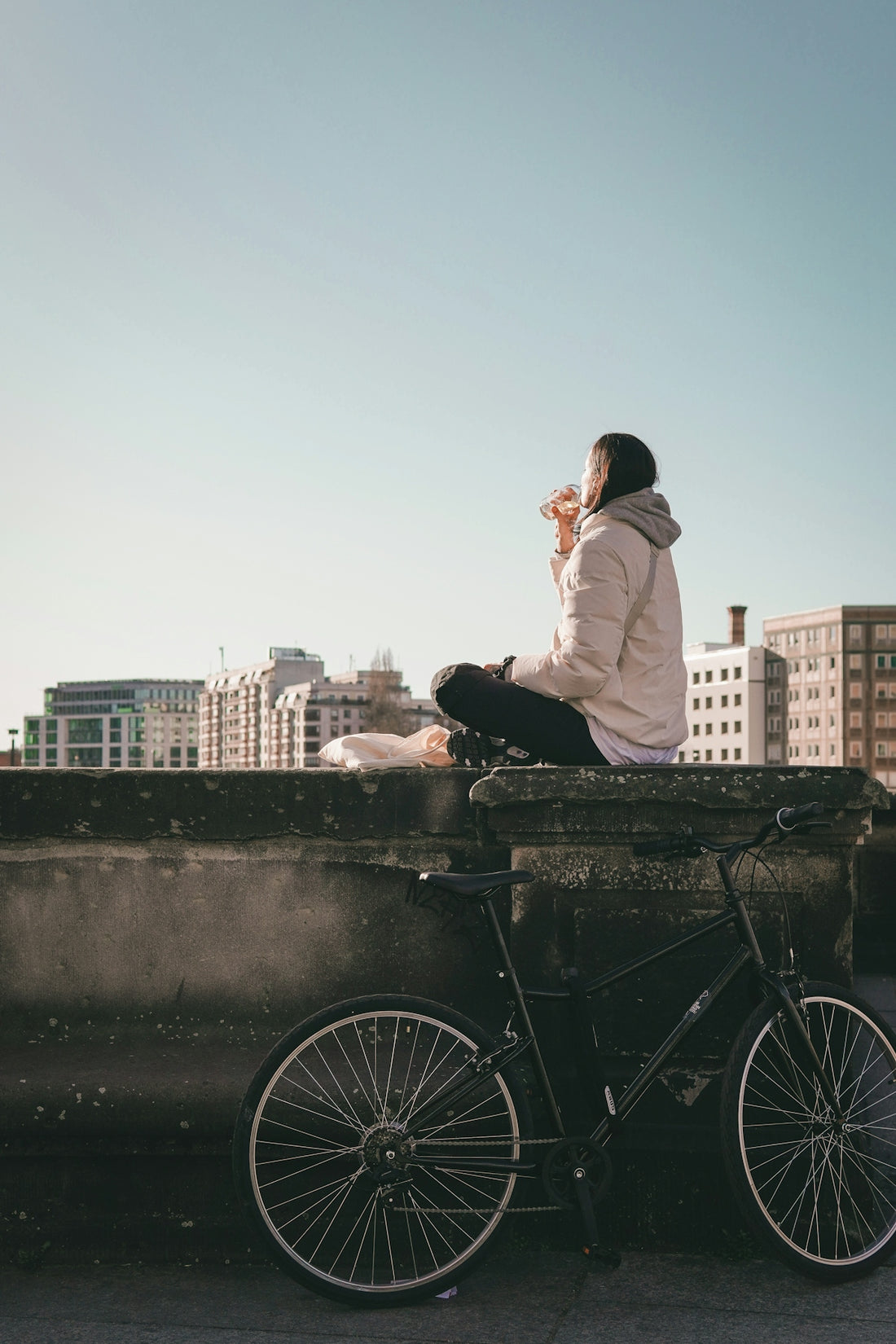 Woman sitting on wall with bicycle and city