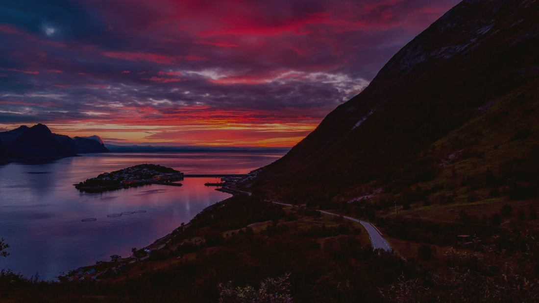 Vivid purple and red sunset over calm lake, island village, and mountain landscape