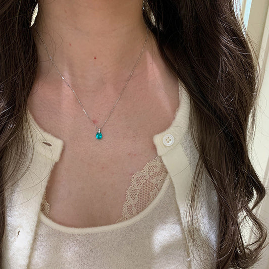 Blue teardrop necklace worn with a cream lace-trim top