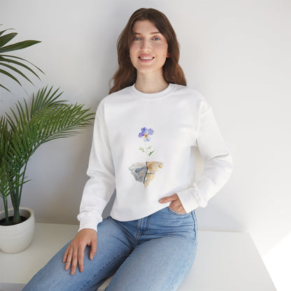Woman in white sweatshirt with watercolor flower and stone design, sitting by a potted plant