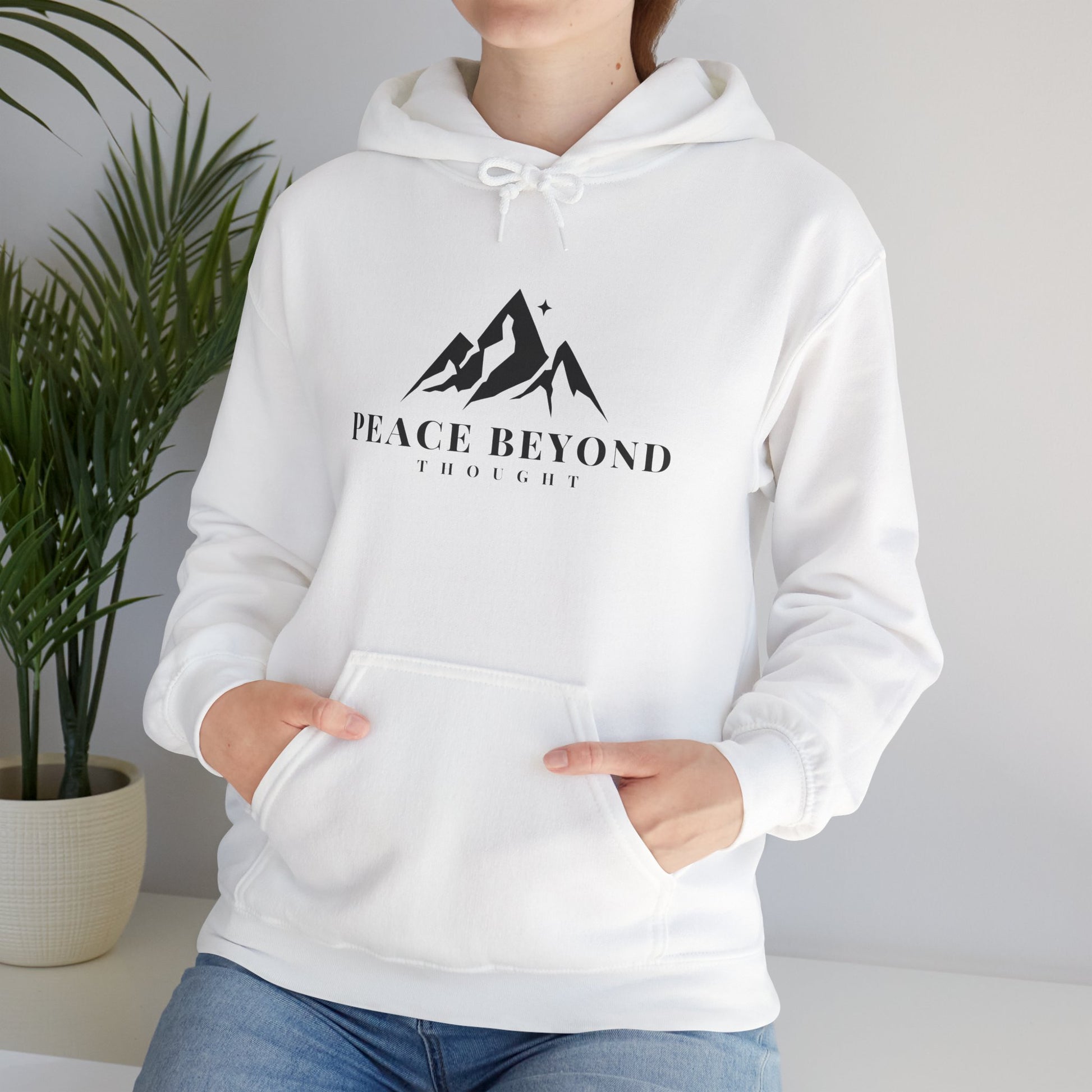 Woman wearing white hoodie with mountain graphic and 'Peace Beyond Thought' text, casual setting