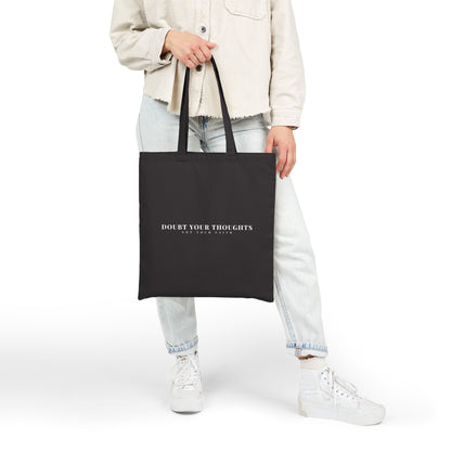 Person holding black tote bag with 'Doubt Your Thoughts Not Your Faith' Christian quote