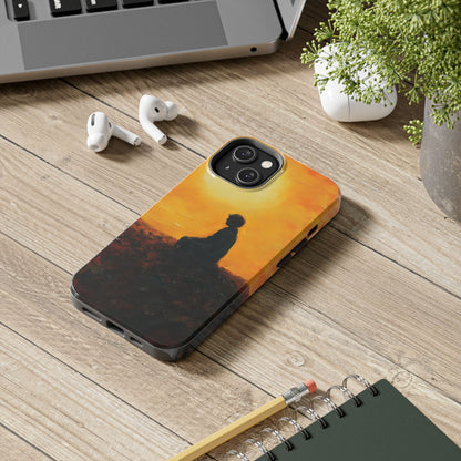 Phone case with meditative silhouette art at sunrise on wood desk near laptop and earbuds