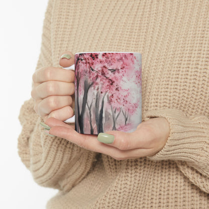 Woman holding ceramic mug with pink cherry blossom tree design, cozy knit sweater visible