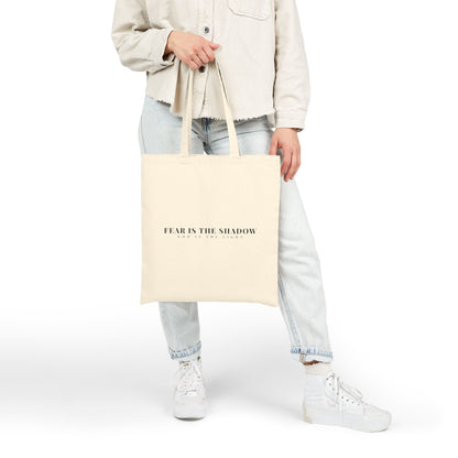 Woman holding a beige Christian tote bag with 'FEAR IS THE SHADOW, GOD IS THE LIGHT' text, casual outfit