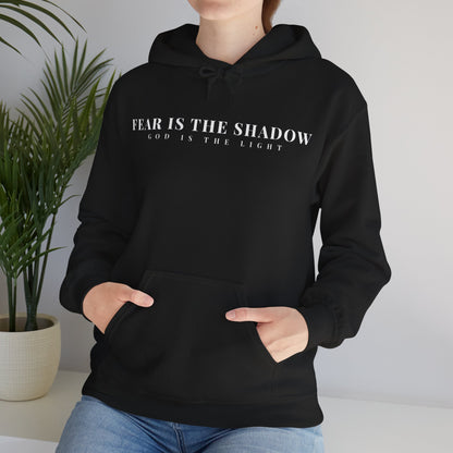 Woman wearing black Christian hoodie with 'Fear is the shadow, God is the light' text, casual home setting