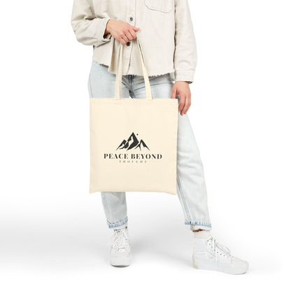 Woman holding beige tote bag with mountain logo and 'Peace Beyond Thought' text, casual outfit