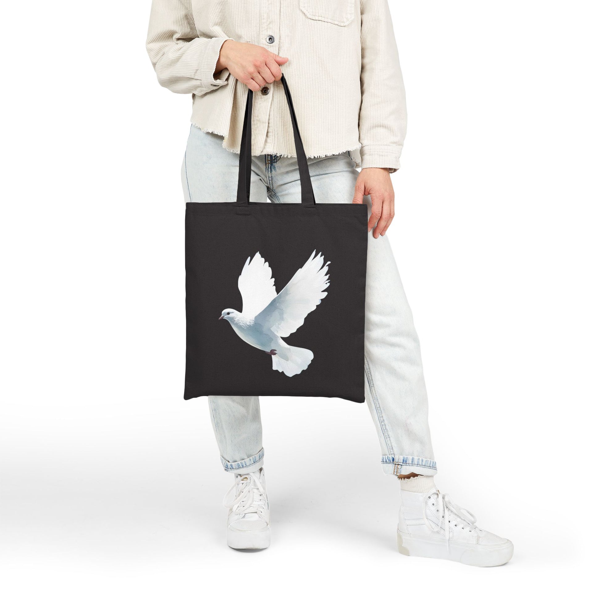 Woman holding black tote bag with white dove Christian art design, casual outfit
