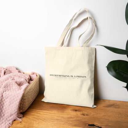 Minimalist beige cotton tote bag with 'Overthinking is a prison' mindful quote on wooden table