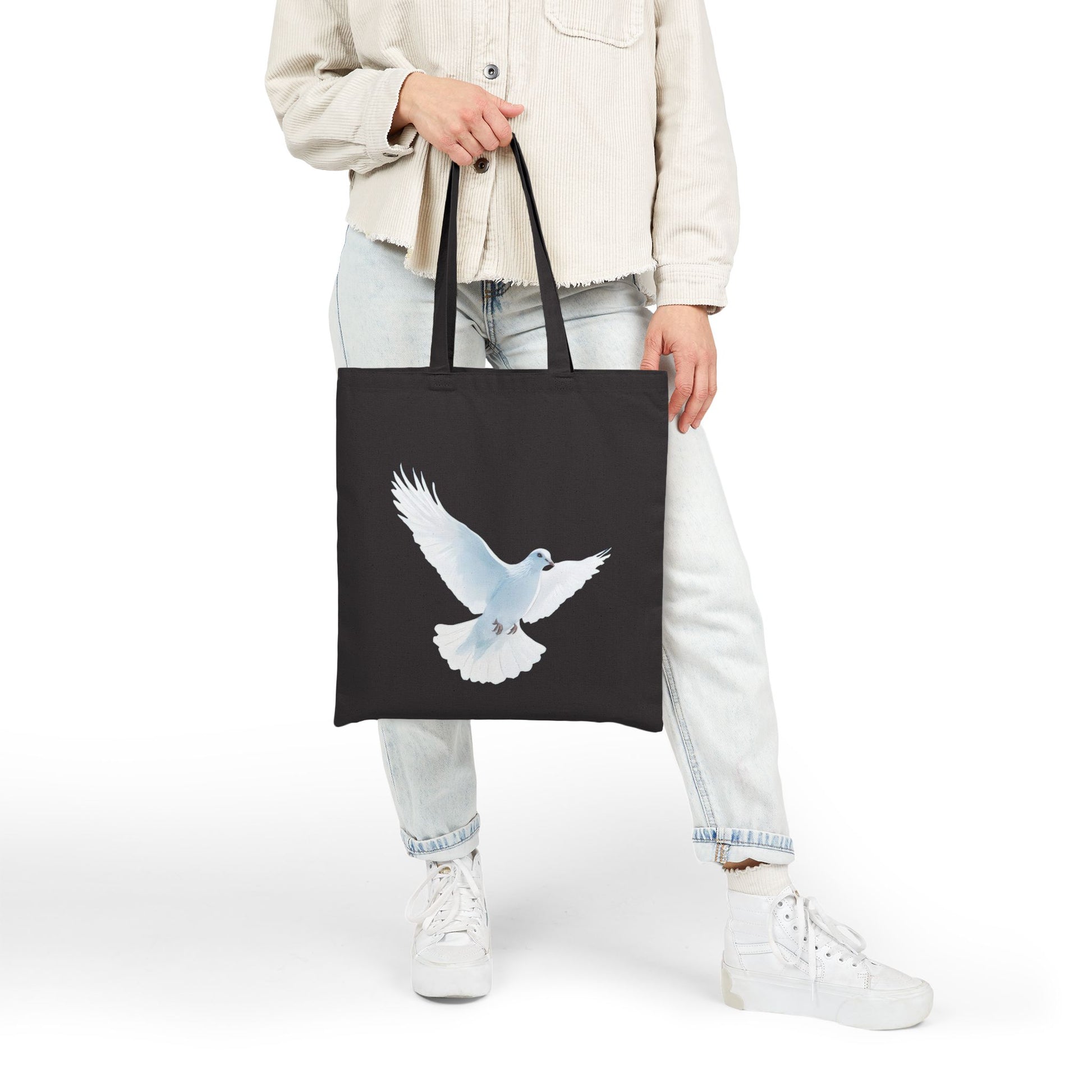 Woman holding black tote bag with white dove design, Christian faith-inspired accessory