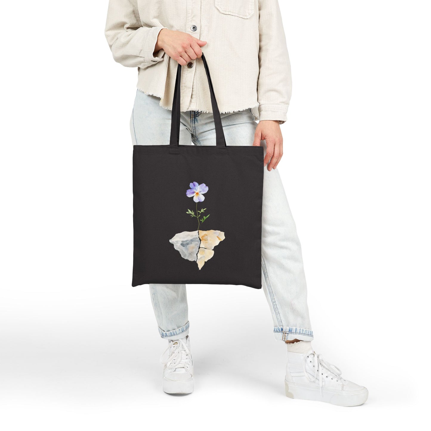 Black tote bag with watercolor flower and stone art, held by person in casual outfit
