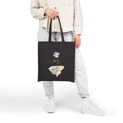 Black tote bag with watercolor flower and stone art, held by person in casual outfit