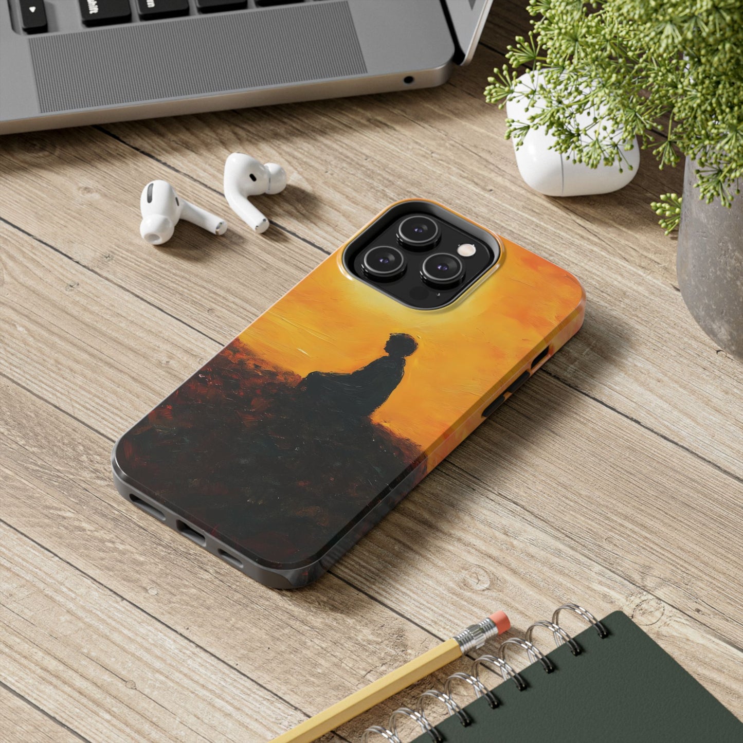 Phone case with silhouette of meditating person against orange sunset on wooden desk