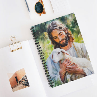 Christian spiral notebook with painting of Jesus holding a lamb, on a white desk with accessories