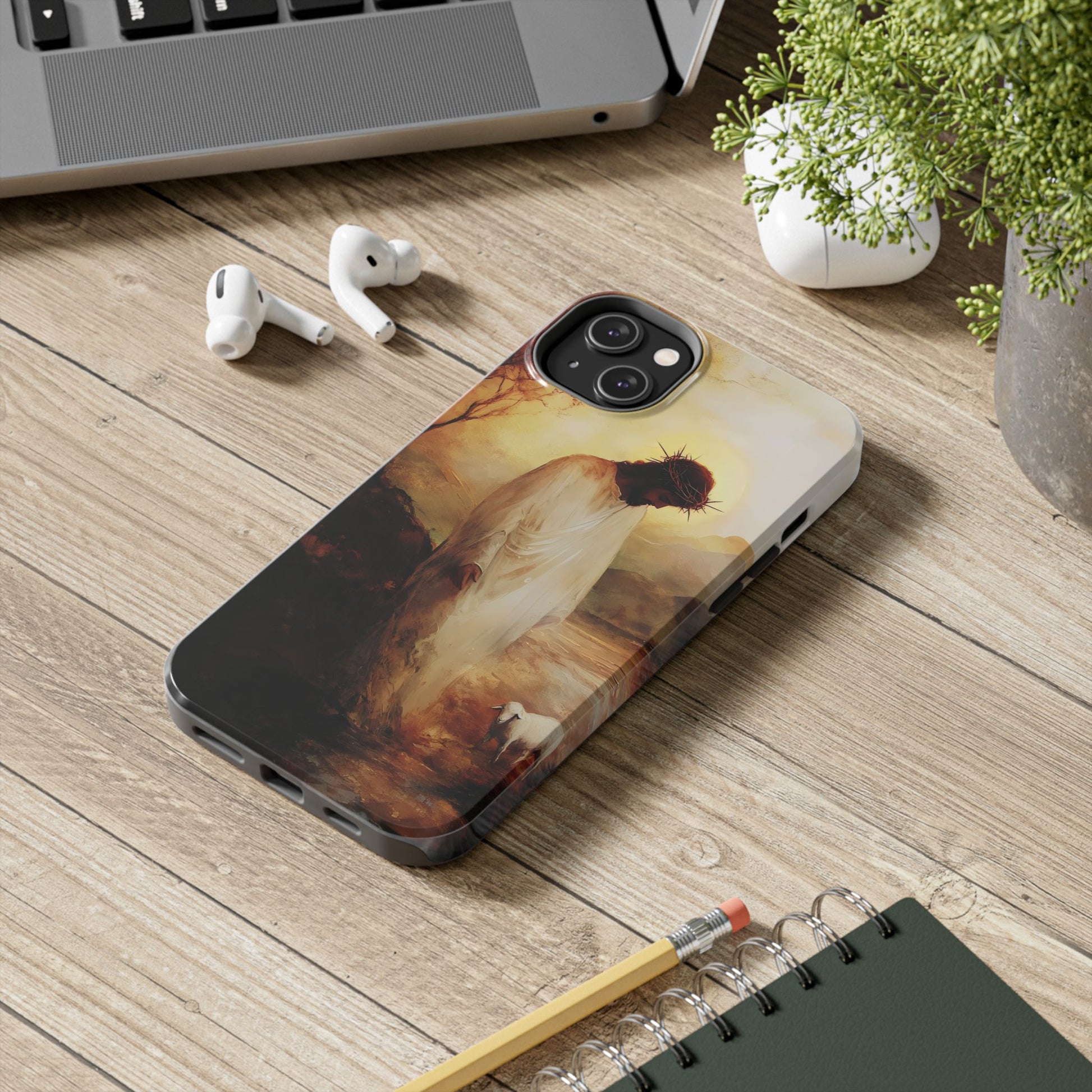 Christian phone case with artistic depiction of Jesus and lamb on wooden desk near laptop