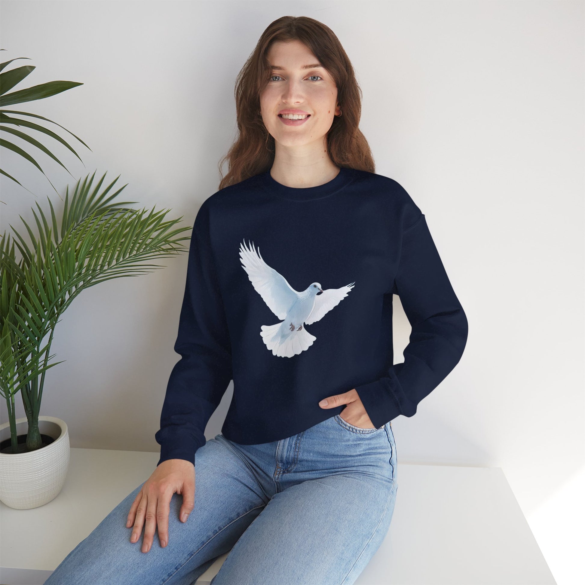 Woman wearing navy Christian sweatshirt with white dove graphic, sitting indoors by plant