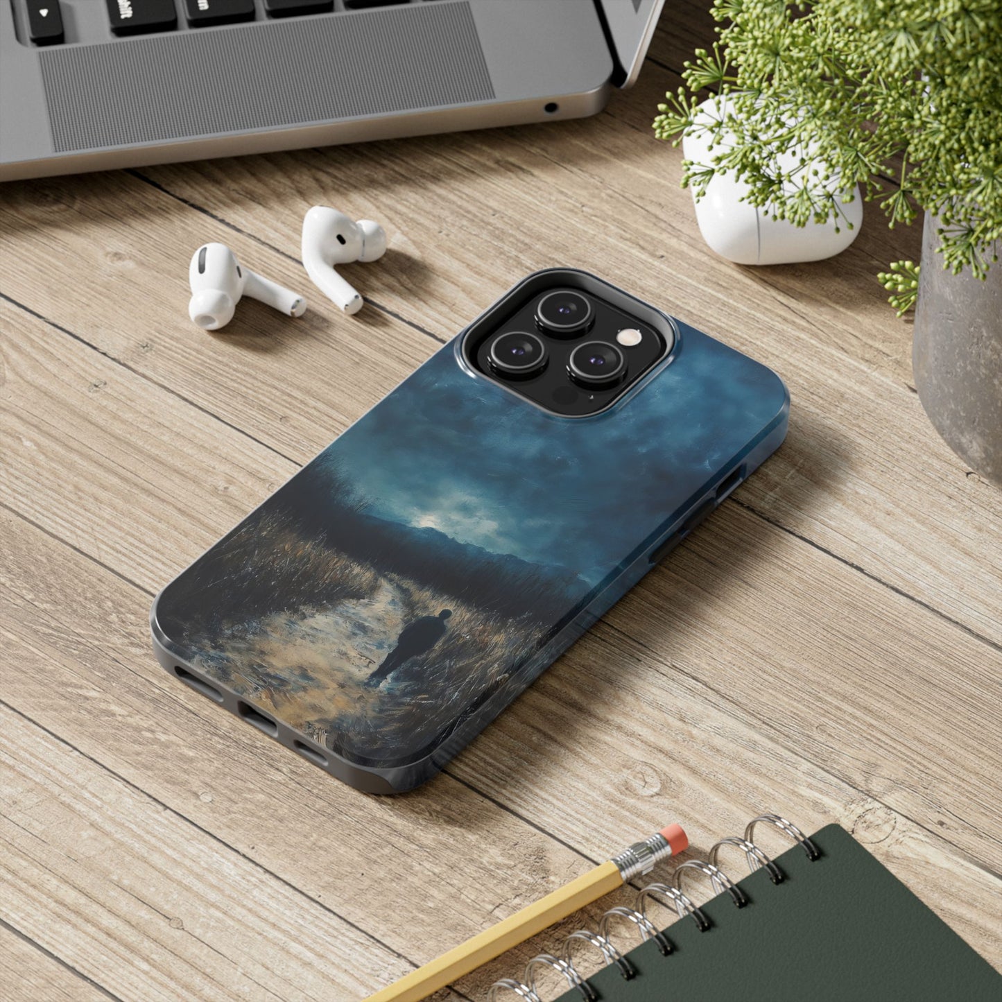 Artistic phone case with contemplative landscape design on wooden desk near laptop and earbuds