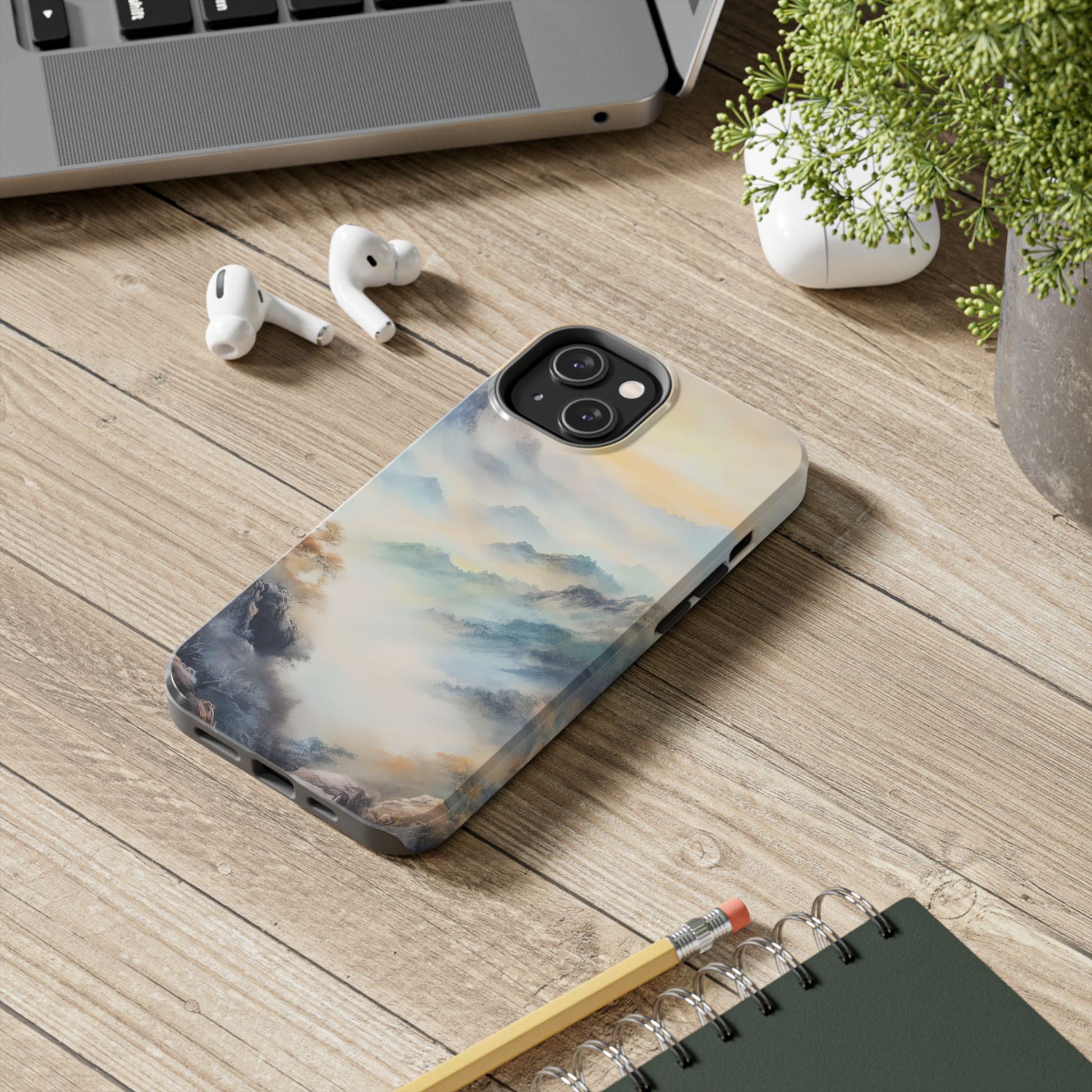 iPhone with serene mountain landscape case on wooden desk, next to AirPods and a notebook