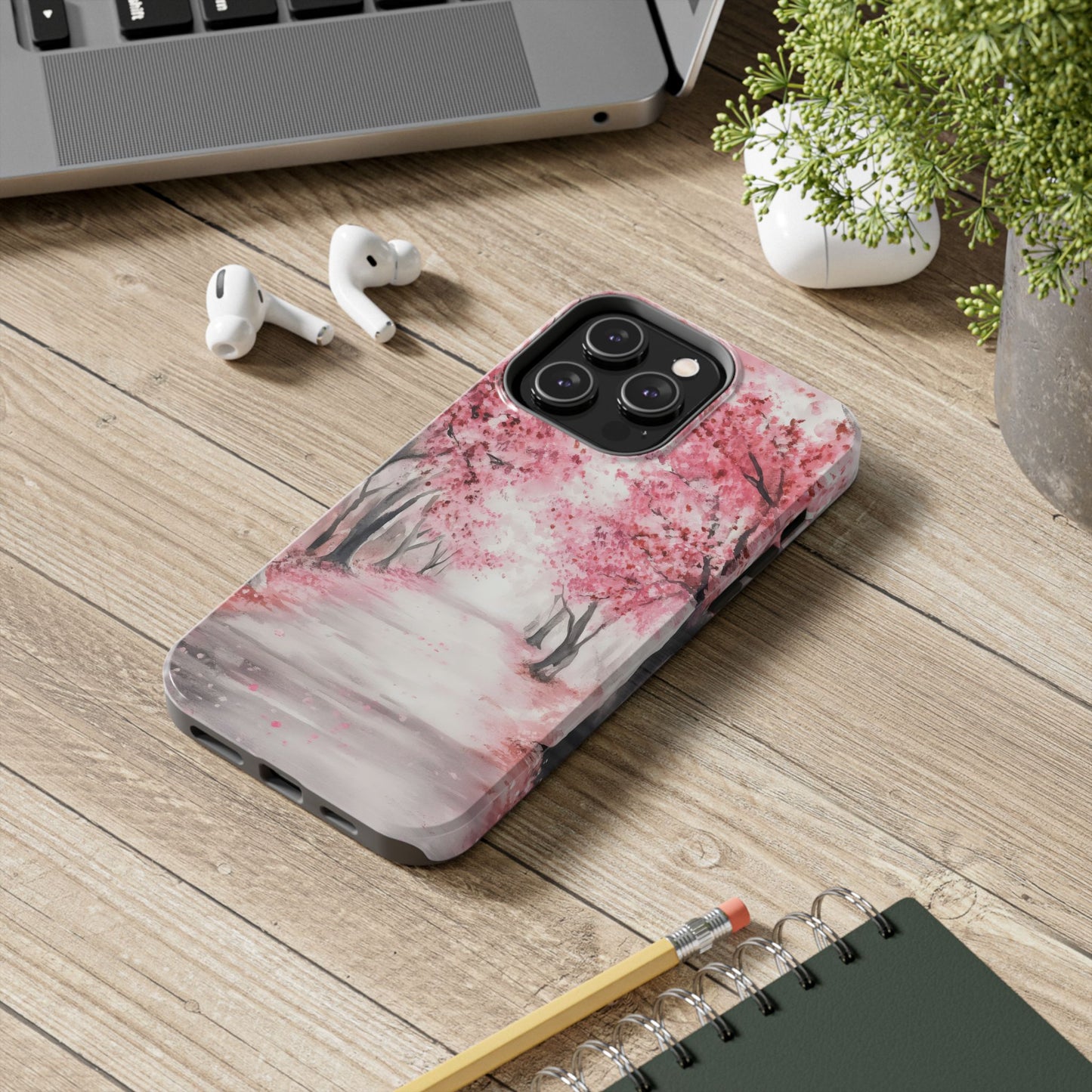 iPhone case with pink cherry blossom trees design on desk with AirPods and notebook