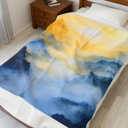 Bed with a soft blanket featuring blue and yellow abstract mountain and sky watercolor design
