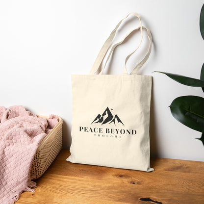 Natural cotton tote bag with mountain graphic and 'Peace Beyond Thought' text on wooden table