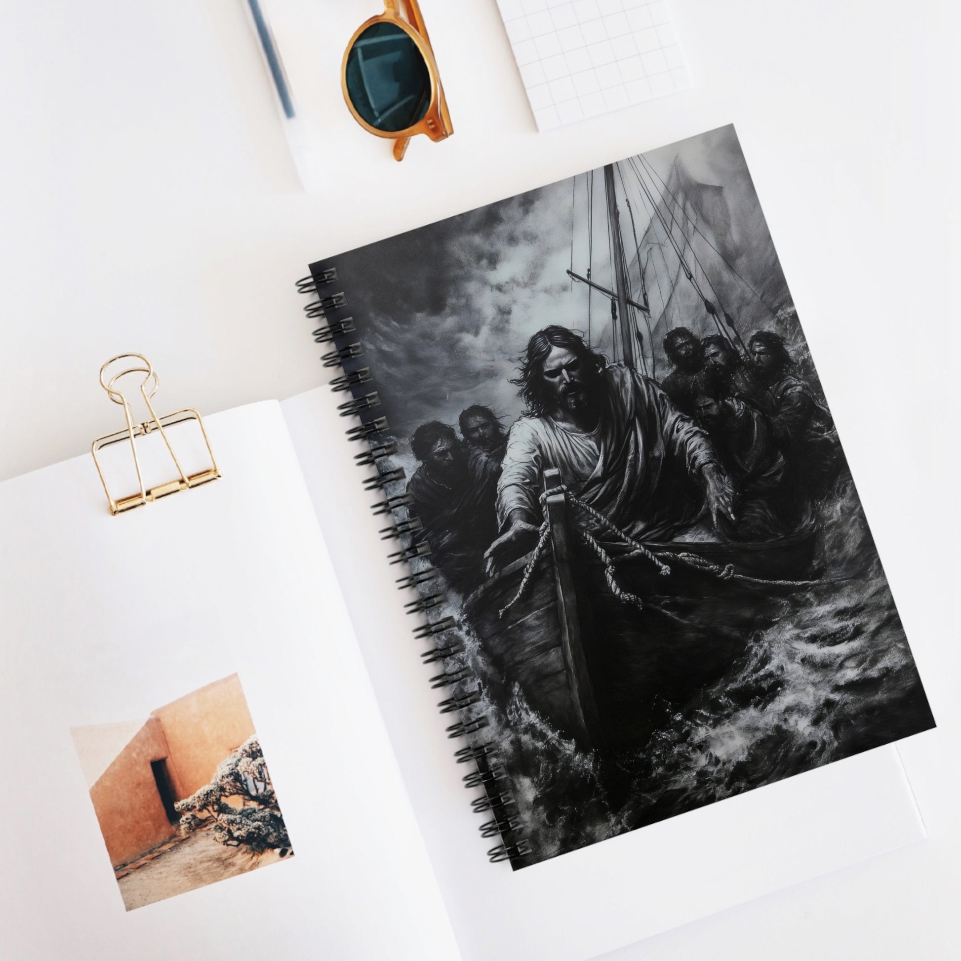 Christian-themed notebook with Jesus calming the storm artwork on desk, surrounded by stationery