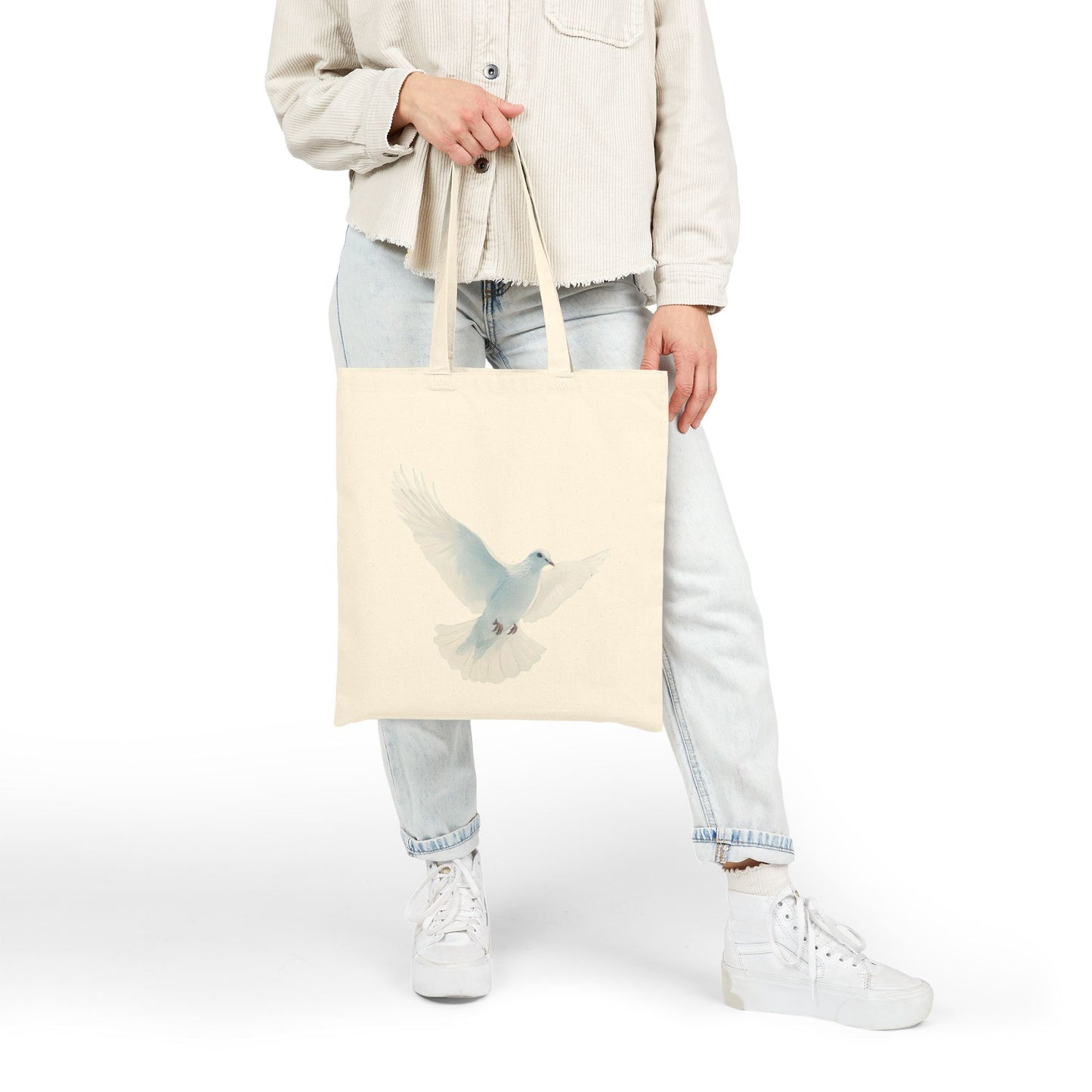 Woman holding a beige tote bag with a white dove illustration, casual faith-inspired fashion