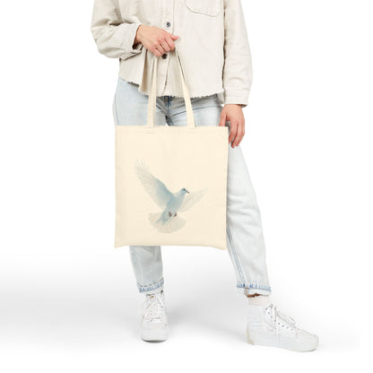 Woman holding a beige tote bag with a white dove illustration, casual faith-inspired fashion