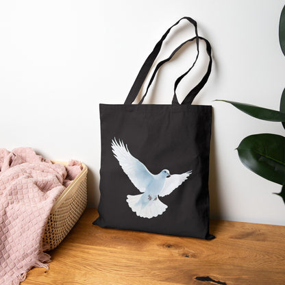 Black tote bag with white dove illustration, Christian gift, on wood table by blanket basket