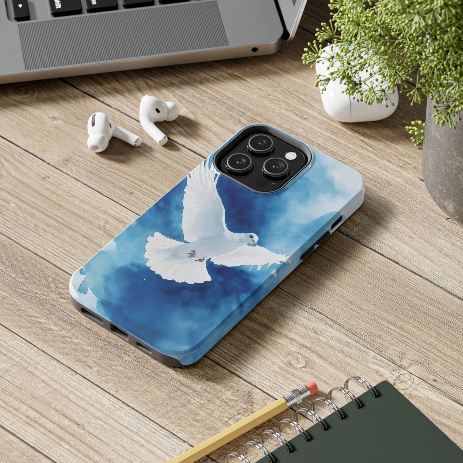 Christian phone case with white dove illustration on blue background, on wooden desk with laptop.