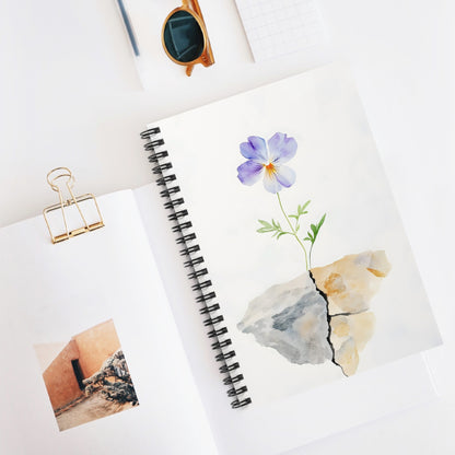 Spiral notebook with watercolor flower growing from cracked stone, minimalist desk scene