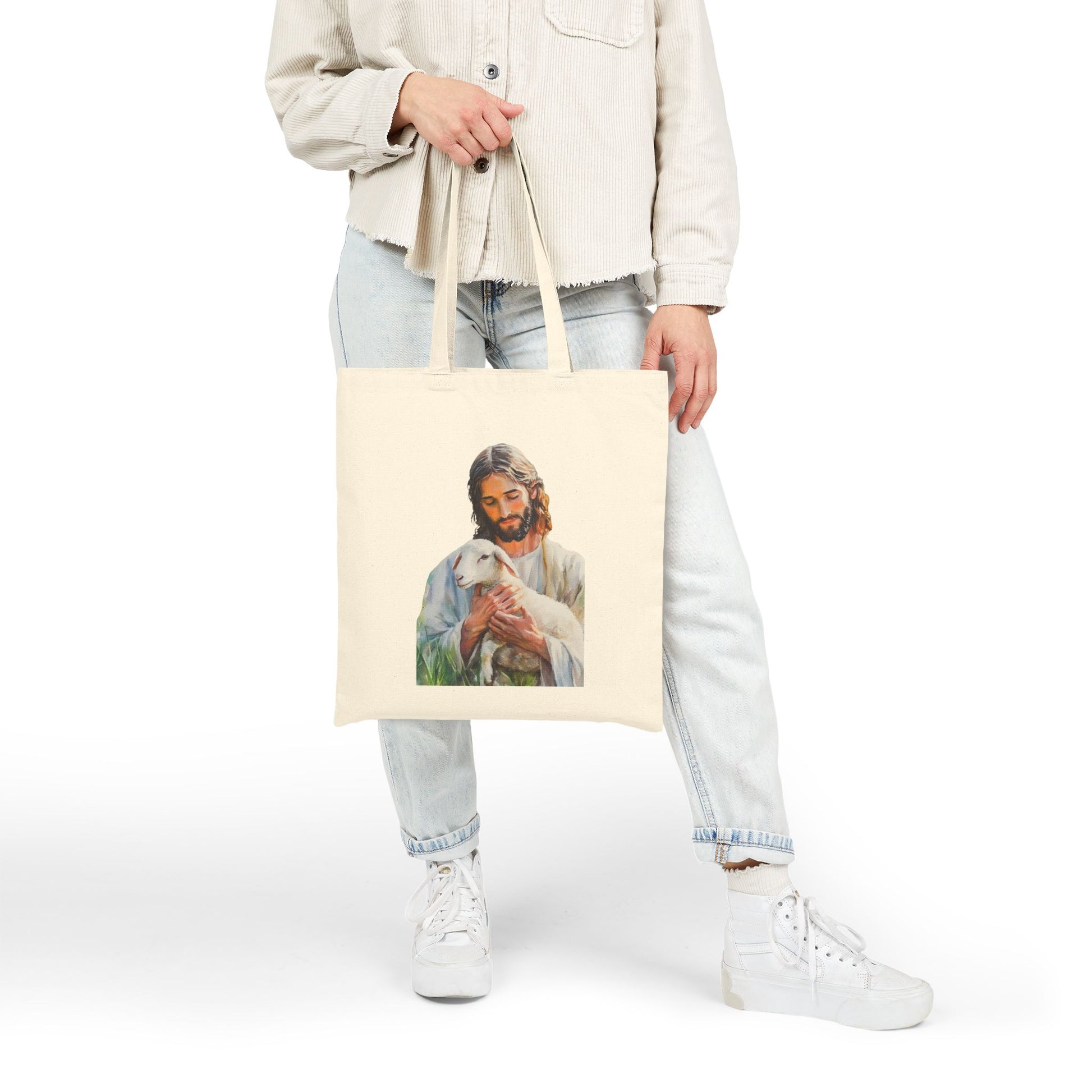 Person holding beige tote bag with Jesus holding lamb Christian art design.