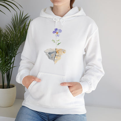 White hoodie with purple flower growing from cracked rock graphic, worn by woman indoors
