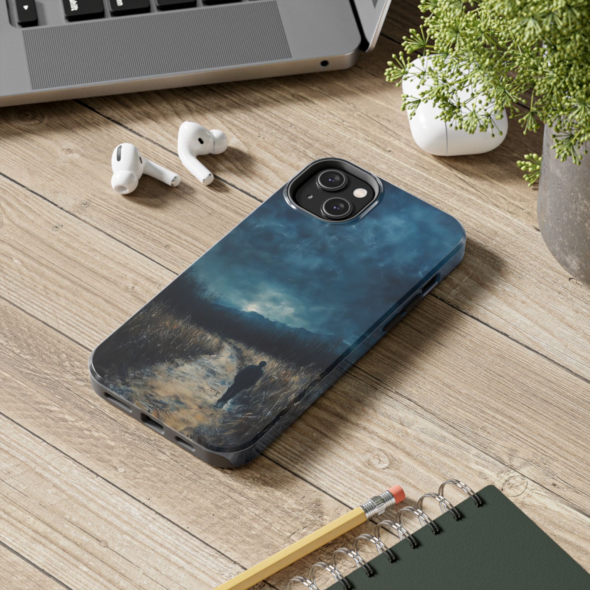 iPhone case with serene spiritual landscape art on wooden desk near laptop, earbuds, and plant