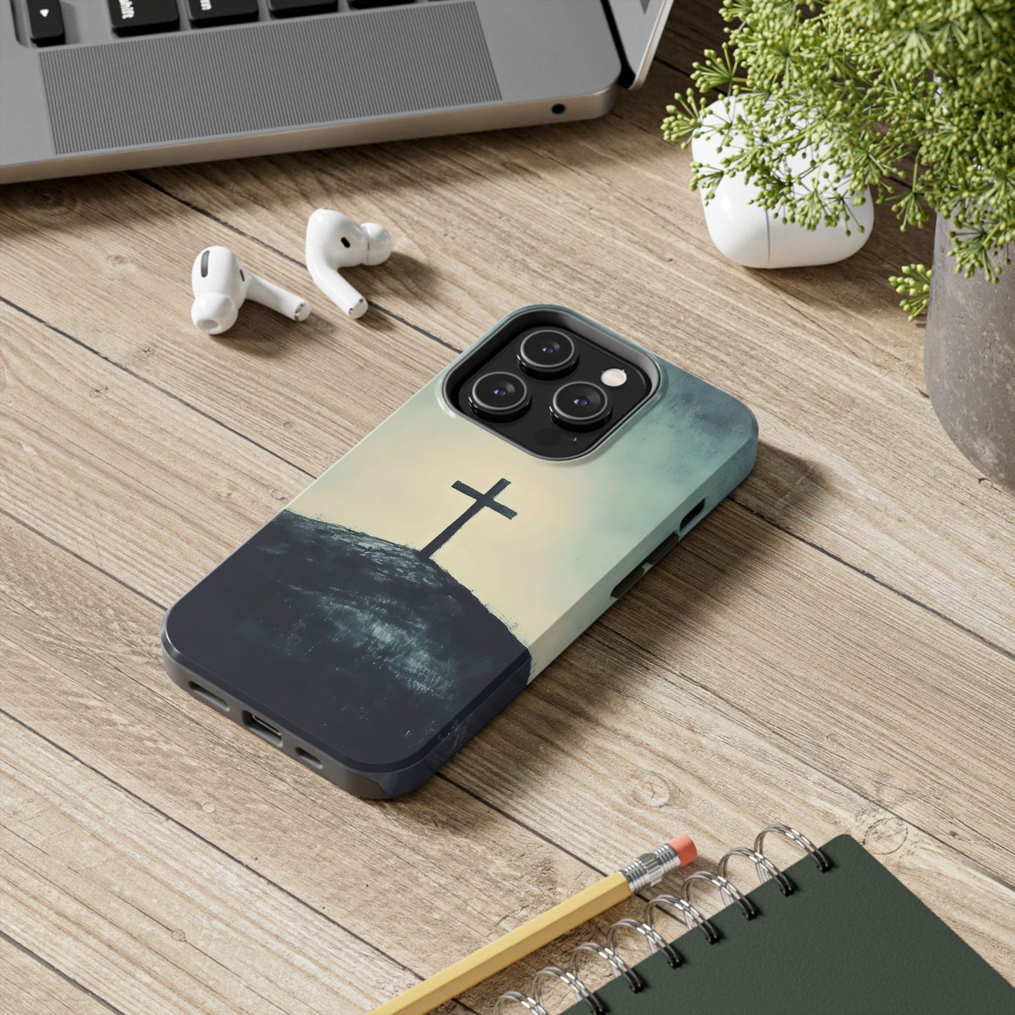 Christian cross phone case on wooden desk with earbuds, laptop, and plant