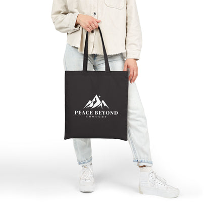 Person holding black tote bag with Peace Beyond Thought mountain logo, casual outfit