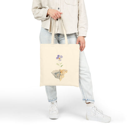 Woman holding canvas tote bag with watercolor flower growing from rock, faith-inspired design