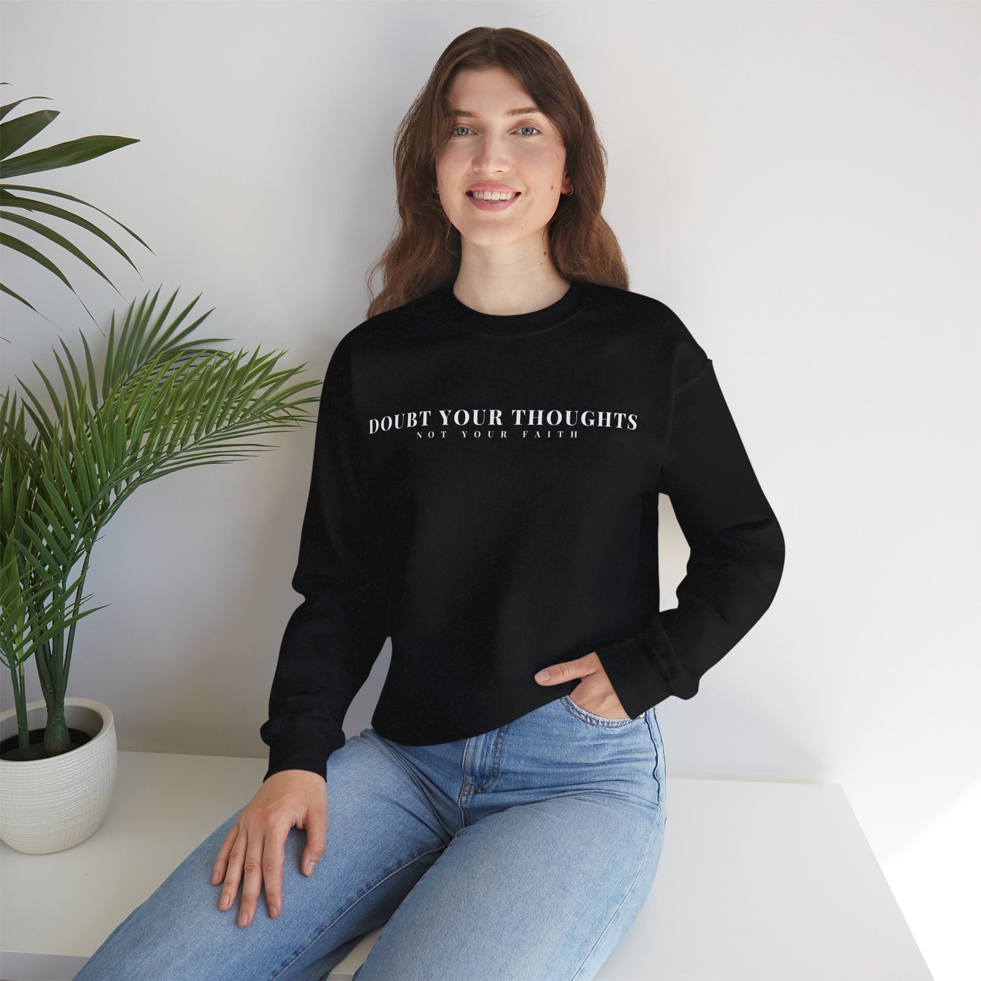 Woman in black Christian sweatshirt with 'Doubt Your Thoughts Not Your Faith' text, sitting in modern room