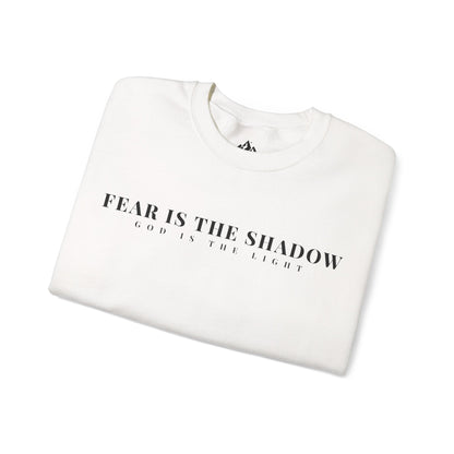Folded white Christian sweatshirt with 'Fear is the shadow, God is the light' text design